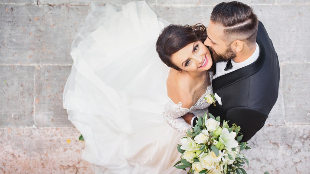 Ein Hochzeitspaar wird von oben fotografiert. Die Braut schaut glücklich nach oben in die Kamera.