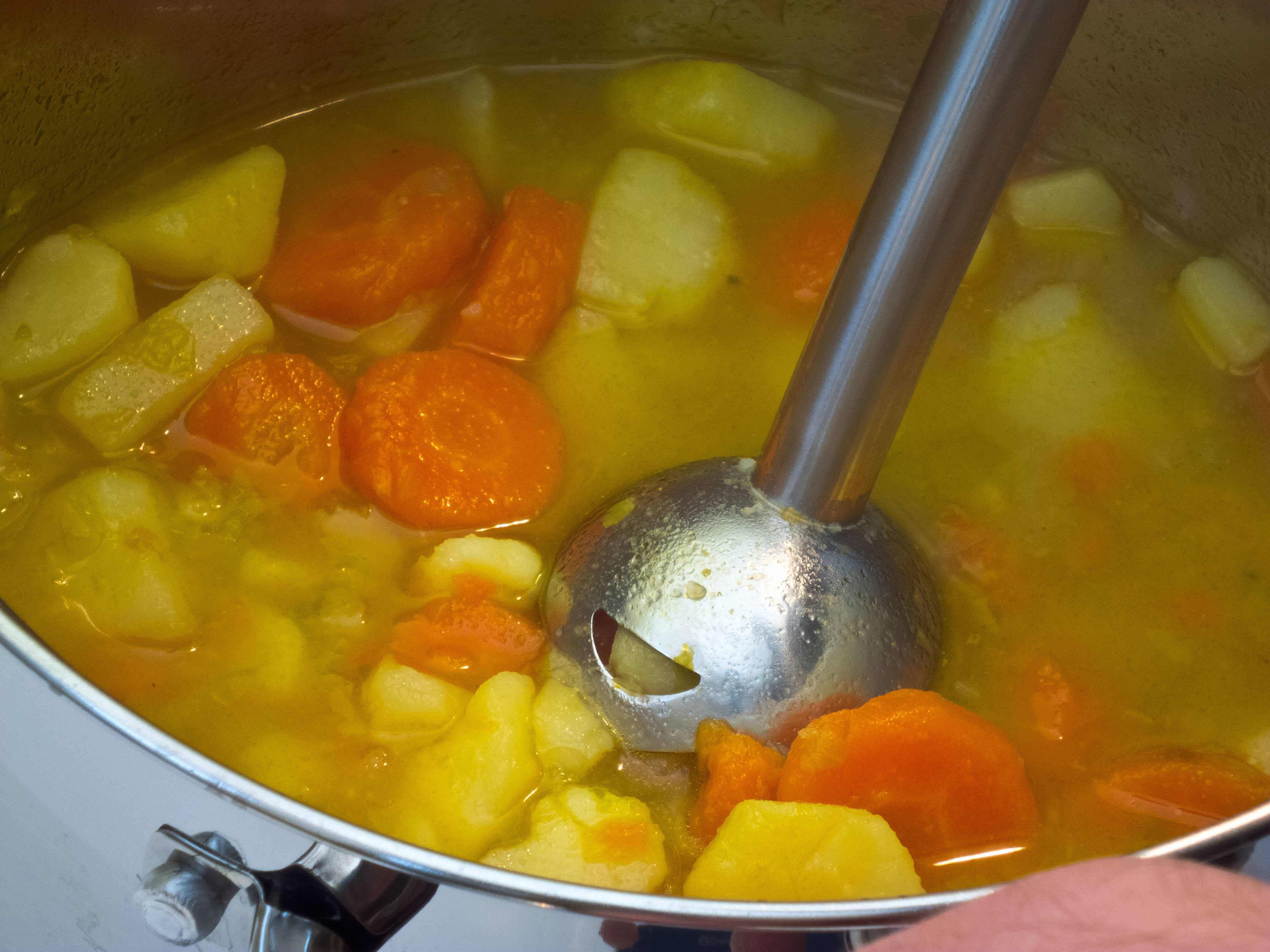 Jemand püriert eine Kartoffelsuppe mit einem Stabmixer.