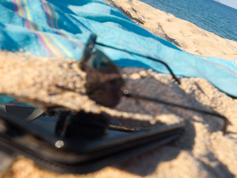 Nahaufnahme von Handy und Sonnenbrille und Handtuch am Strand.