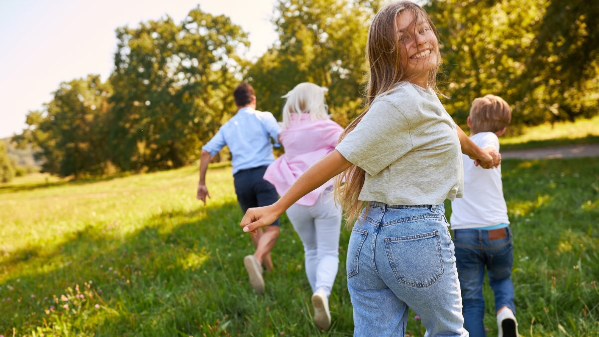 Eine Familie rennt frÃ¶hlich Ã¼ber eine Wiese. Das MÃ¤dchen hinten schaut glÃ¼cklich in die Kamera.