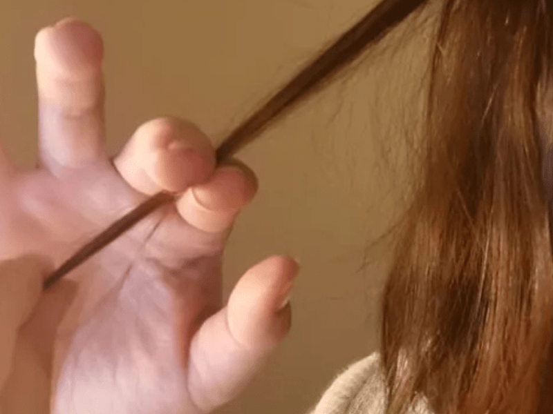 Eine Person mit braunen Haare hält eine Haarsträhne in die Kamera.