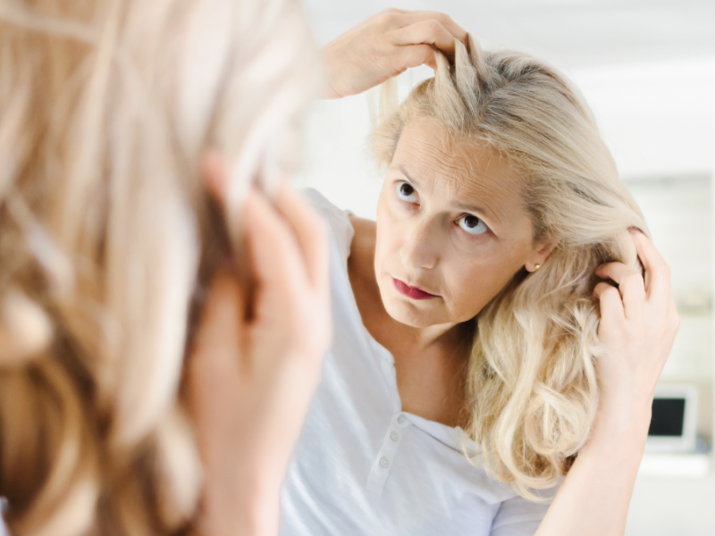 Eine ältere Frau schaut sich im Spiegel ihre langen Haare an.