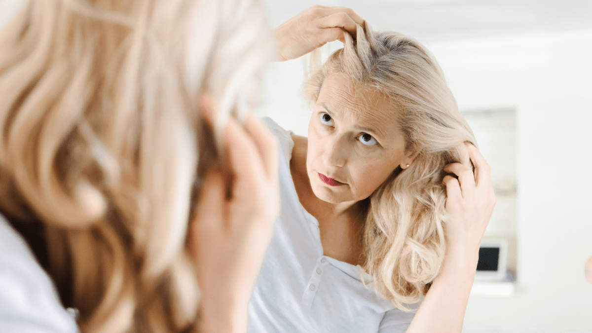 Eine ältere Frau schaut sich im Spiegel ihre langen Haare an.