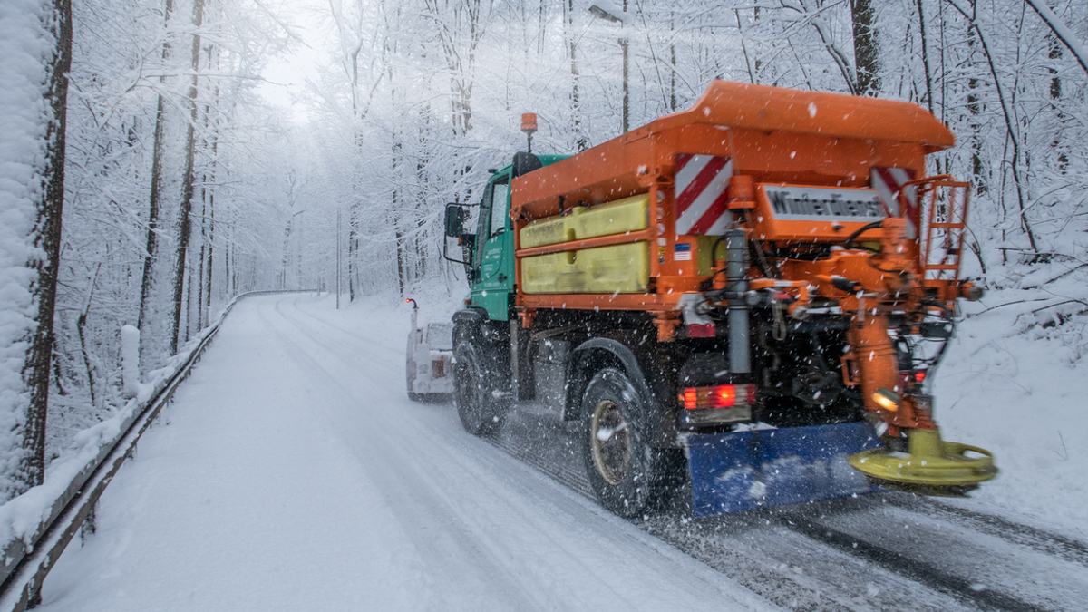 Ein Streuauto auf einer verschneiten StraÃŸe im Wald.