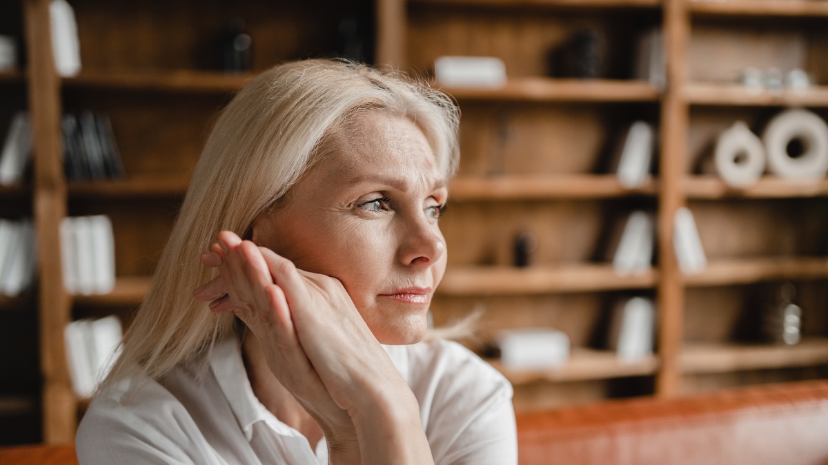 Eine mittelalte Frau mit langen, weiÃŸblonden Haaren schaut nachdenklich in die Ferne.