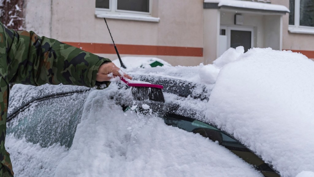 Auto mit einem Handbesen von Schnee befreien.