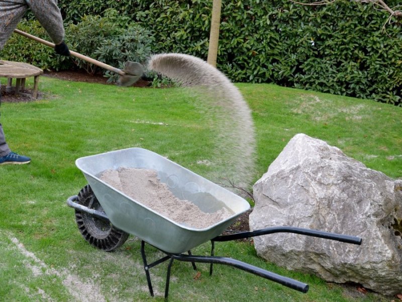 Quarzsand wird mit einer Schaufel auf einem Rasen in einem Garten ausgebracht.