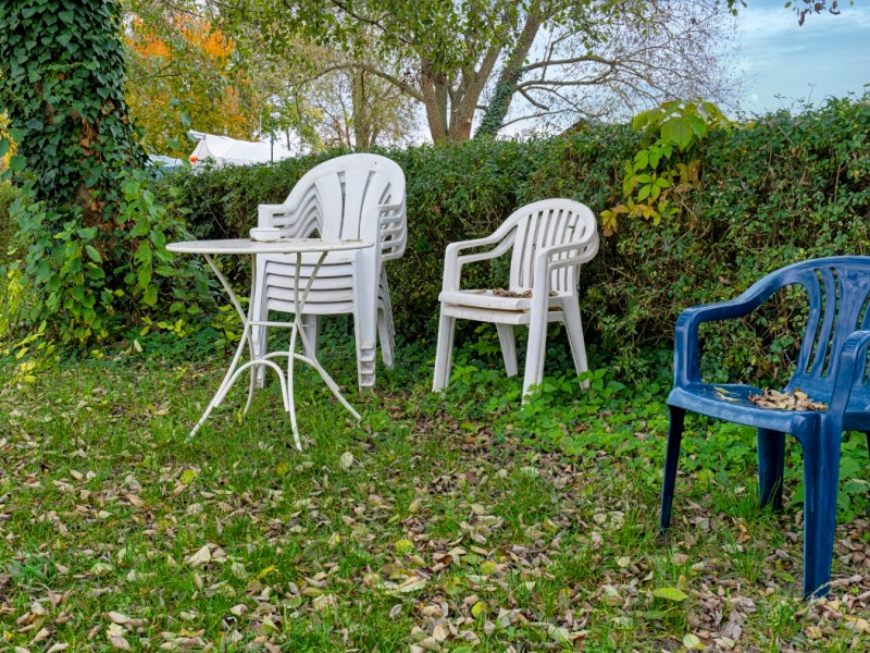 Gartenmöbel und Gartenstühle stehen gestapelt in einem Garten.