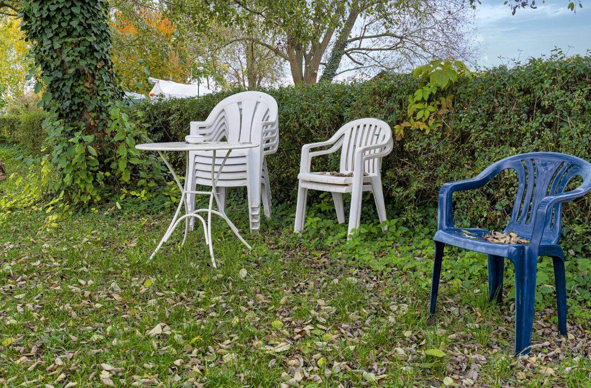 Gartenmöbel und Gartenstühle stehen gestapelt in einem Garten.