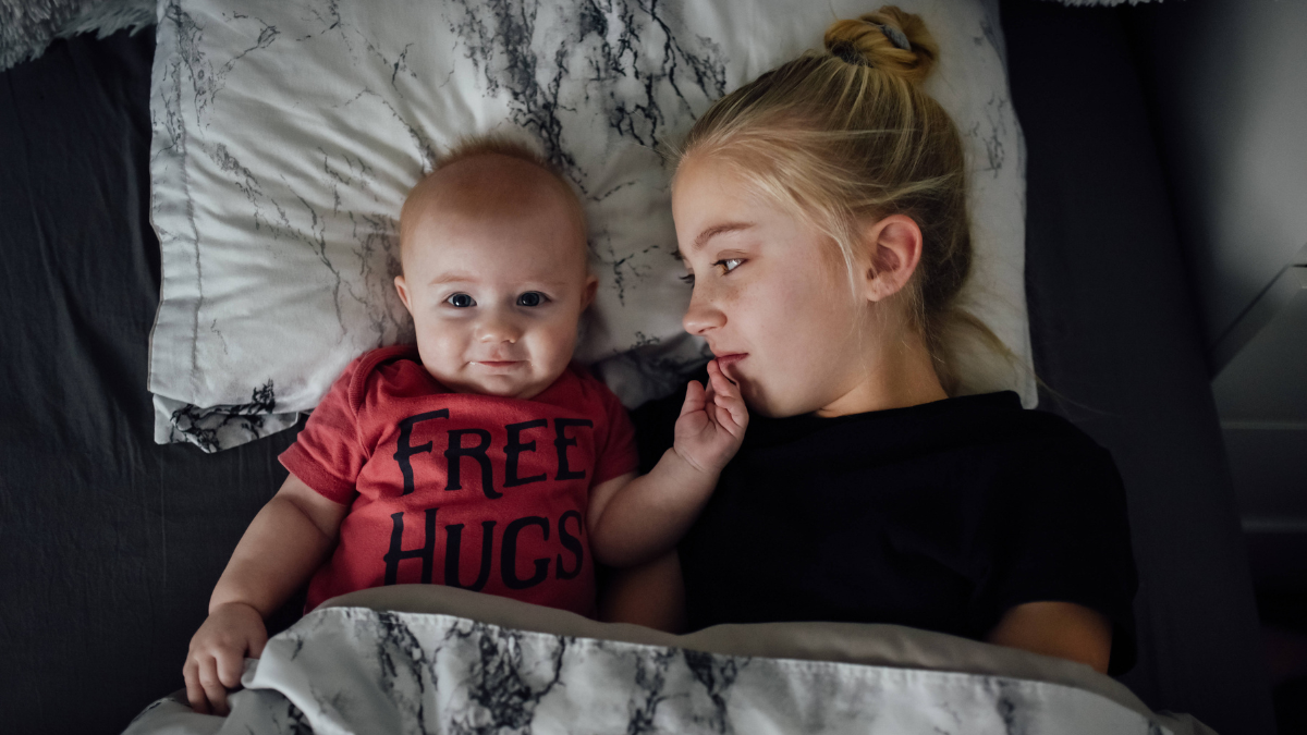 Ein Baby und ein etwas Ã¤lteres MÃ¤dchen liegen gemeinsam im Bett.