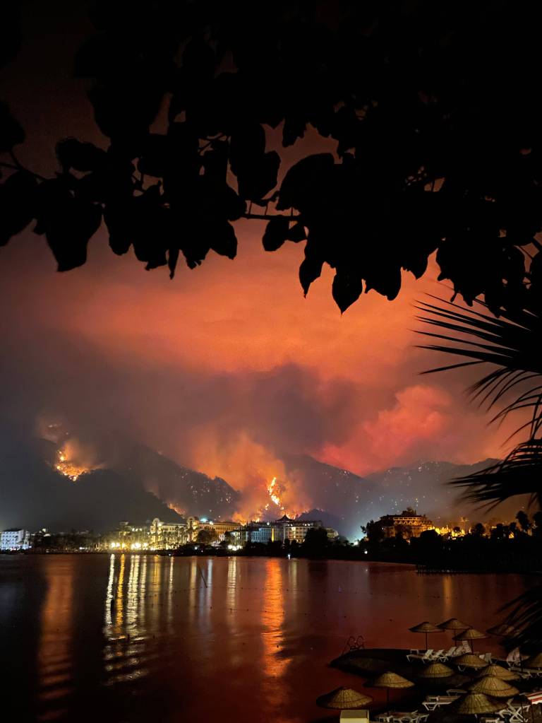 Von einem Feuer rotgefärbter Himmel spiegelt sich im Wasser.