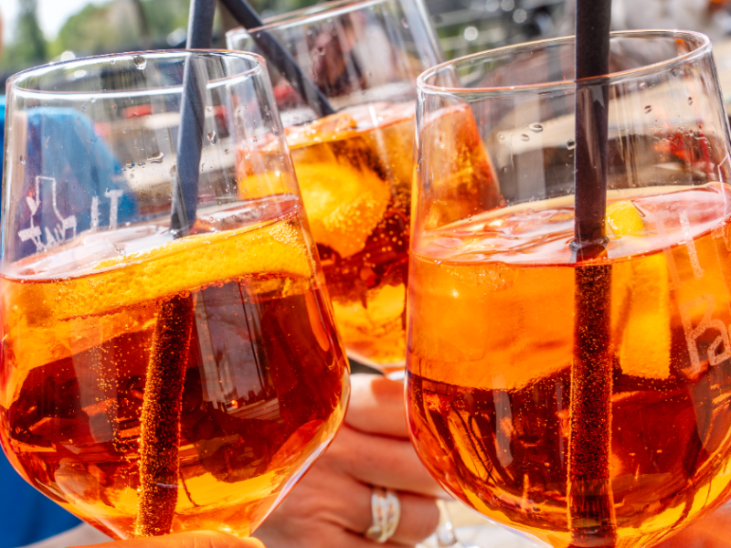 Drei Gläser mit Aperol Spritz in der Sonne.