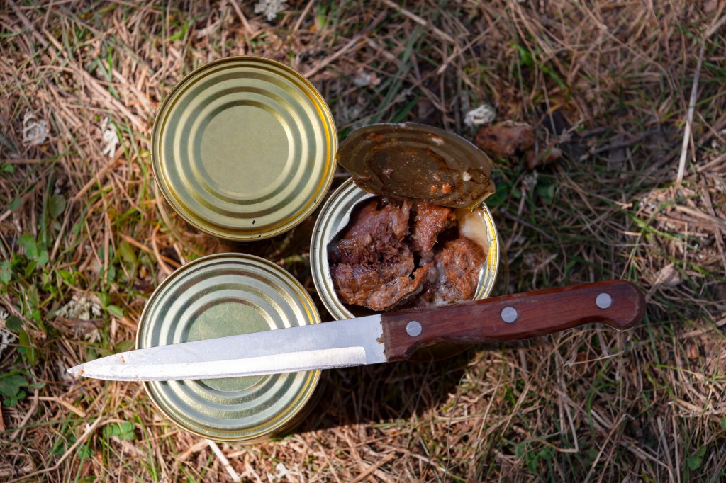 Ein Messer liegt auf Dosen mit Wildfleisch, eine Dose ist geöffnet.