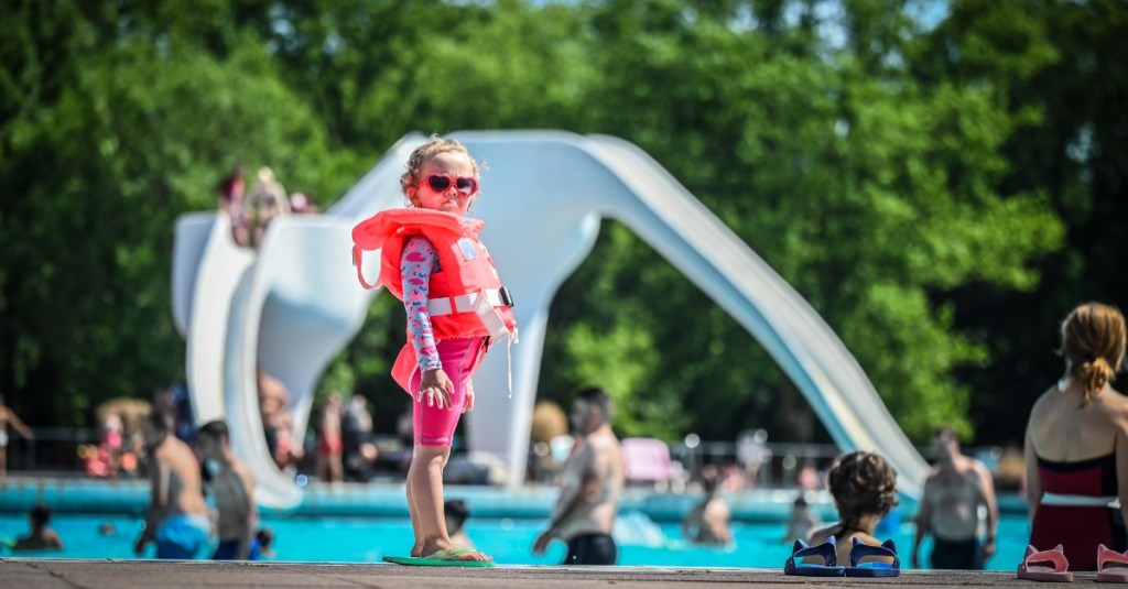 Kleines Mädchen steht skeptisch in Kinder-Schwimmlernweste am Beckenrand