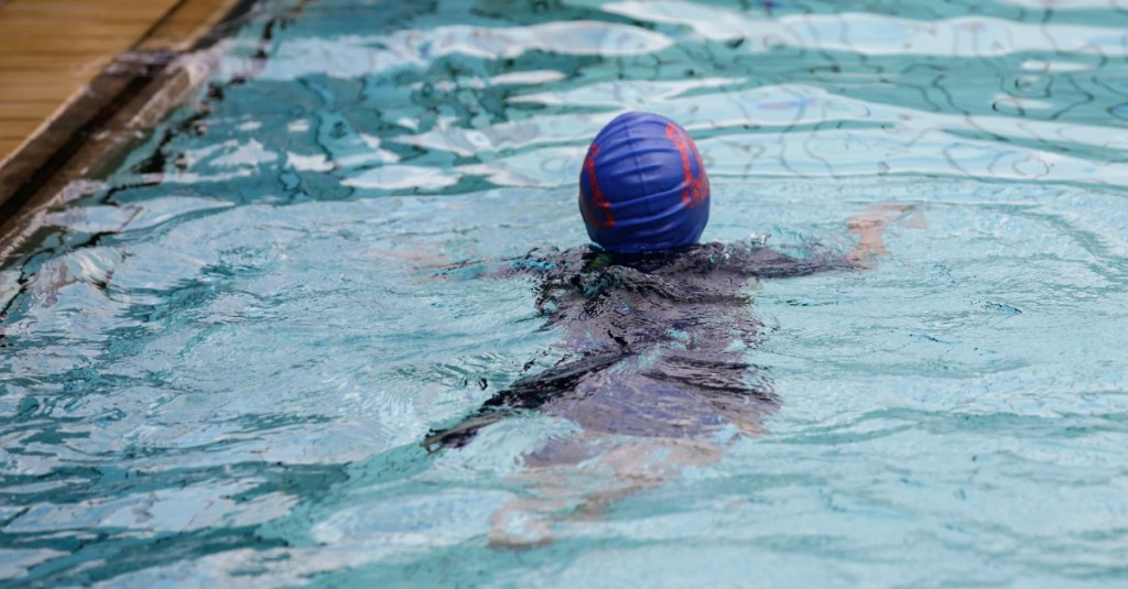 Kind mit Badekappe schwimmt in einer Schwimmhalle