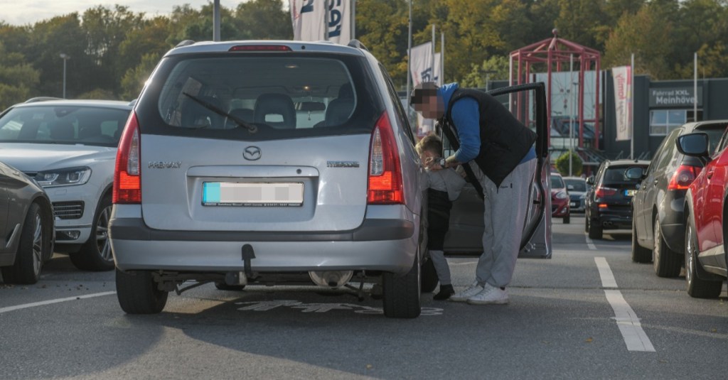 Ein Vater steigt mit seinem Sohn auf einem Eltern-Kind-Parkplatz in ein Auto.