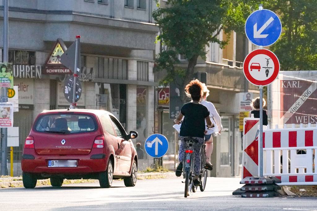 Ein PKW überholt zwei Radfahrer trotz Überholverbot, das von dem Straßenschild 277.1 angezeigt wird.