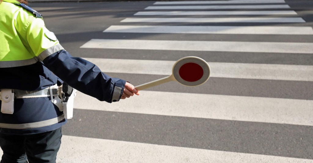 Polizist steht an einem Zebrastreifen und kontrolliert, ob die Verkehrsregeln eingehalten werden.