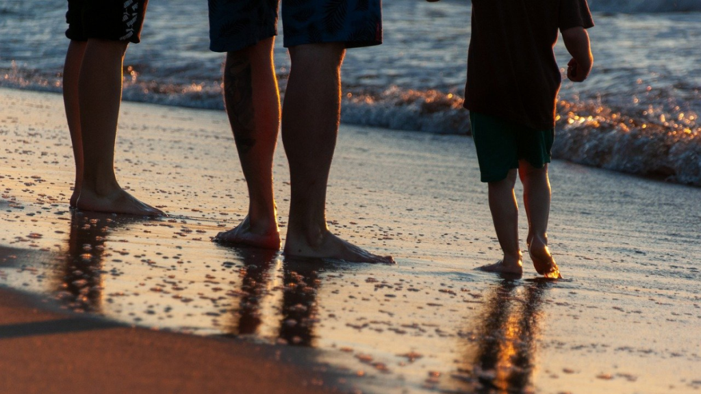 Die Füße dreier Menschen, die beim Sonnenuntergang am Strand entlanglaufen.