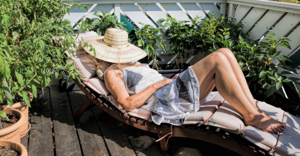 Frau sonnt sich auf einem Balkon, ein Hut verdeckt ihr Gesicht.
