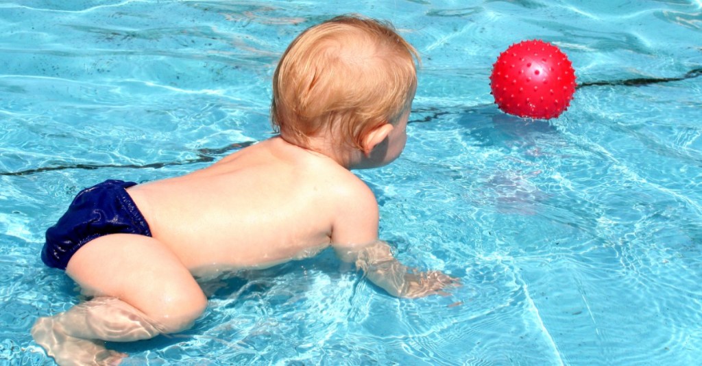 kleines Baby in blauer Badehose plantscht im Wasser