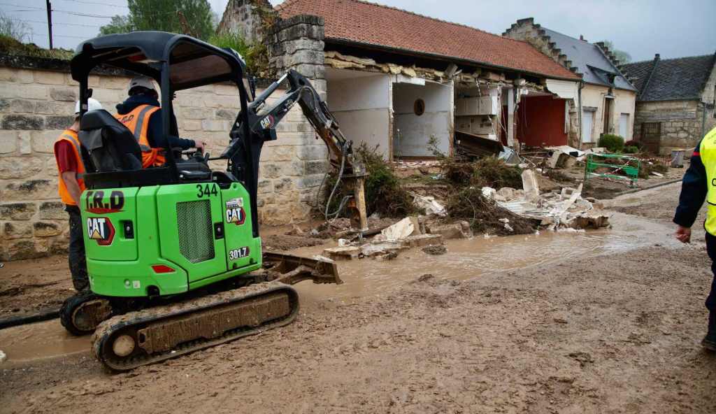 Ein Bagger vor einem durch Sturmschäden zerstörten Haus.