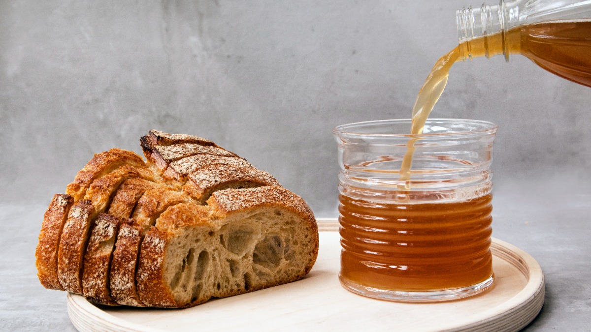 Ein Laib Brot und daneben steht ein Glas, in das eine brÃ¤unliche FlÃ¼ssigkeit gegossen wird.