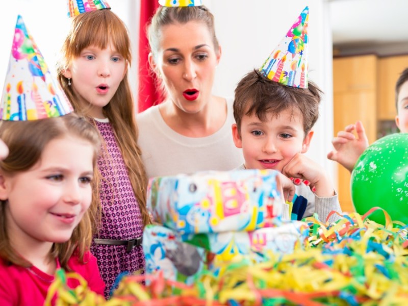 Kleine Kinder mit Partyhüten sitzen an einem Geburtstagstisch