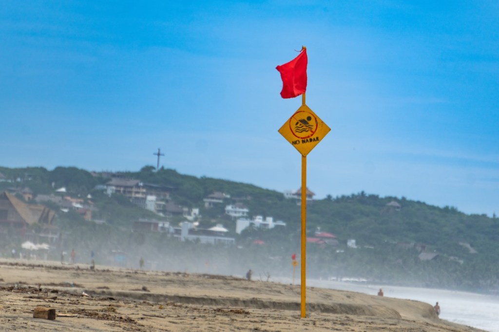 Ein Strand mit einem Schild und einer roten Flagge.