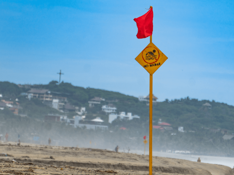 Ein Strand mit einem Schild und einer roten Flagge.