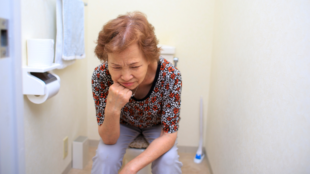 Eine Frau sitzt mit schmerzverzerrtem Gesicht auf der Toilette.