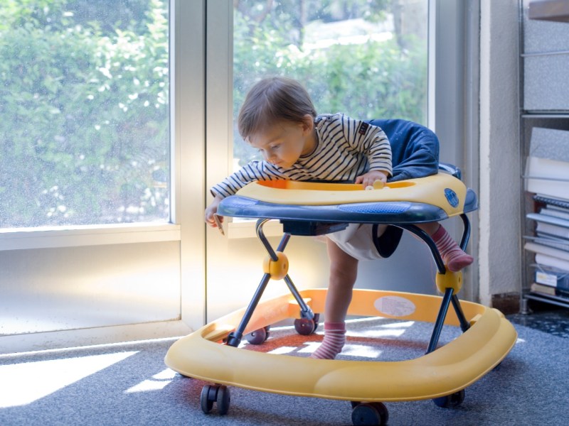 Ein Kleinkind spielt in einem Babywalker, einem sogenannten Gehfrei.