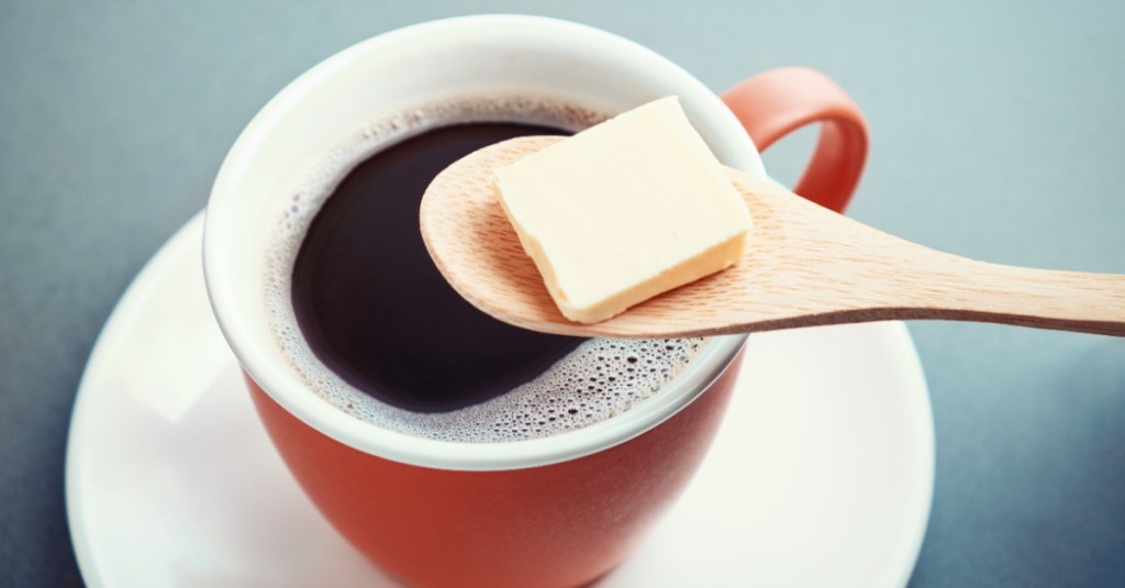 eine rote Tasse mit Kaffee, darauf liegt ein Löffel mit einem Stück Butter