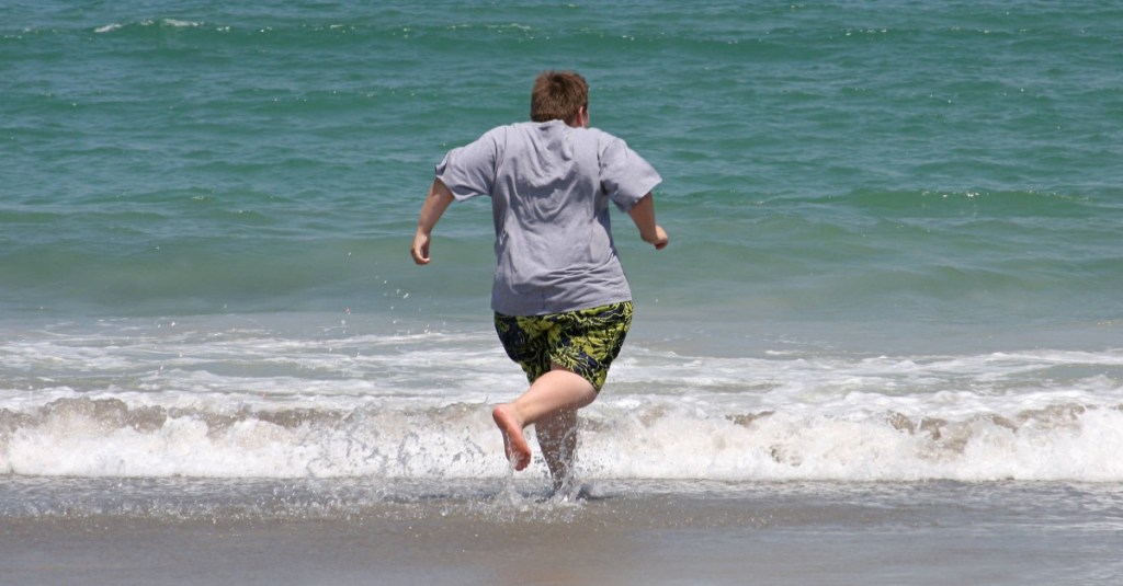 Ein übergewichtiger Junge rennt am Strand entlang