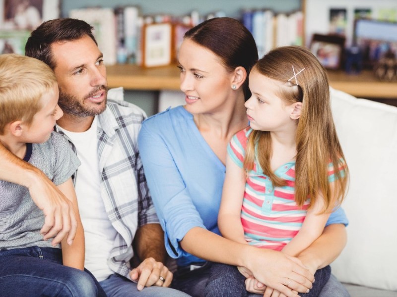 Vater, Mutter und zwei Kinder sitzen gemeinsam auf dem Sofa