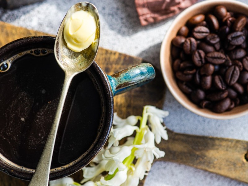 Auf einer Tasse Kaffee liegt ein Löffel mit etwas Butter