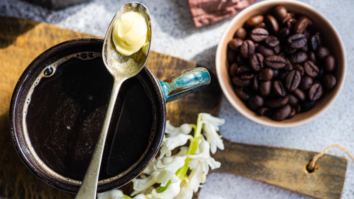 Auf einer Tasse Kaffee liegt ein Löffel mit etwas Butter