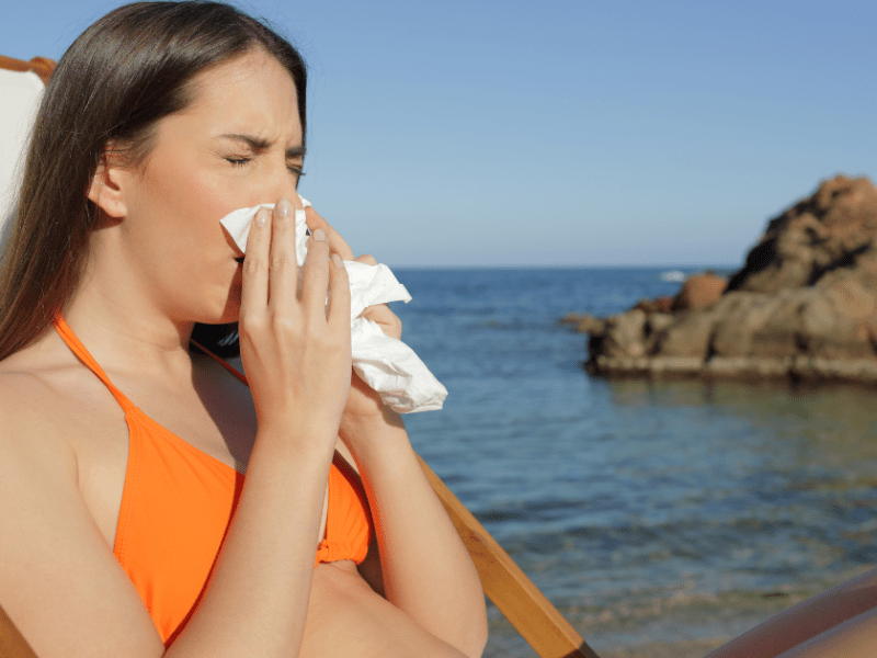 Junge Frau mit Taschentuch ist krank am Strand.