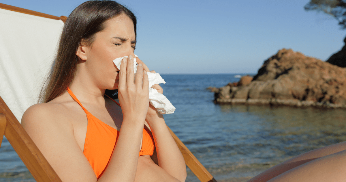 Junge Frau mit Taschentuch ist krank am Strand.