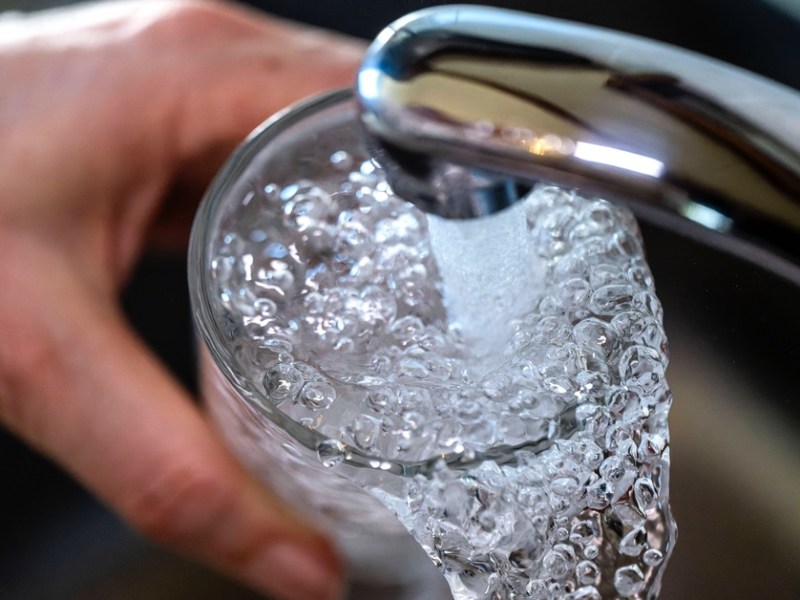 Jemand füllt ein Glas unter dem Wasserhahn mit Leitungswasser.