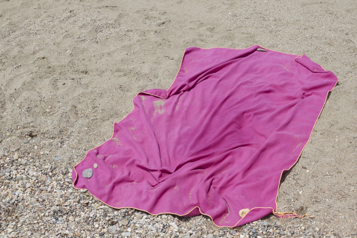 Ein pinkes Handtuch mit Sand an einem Strand.