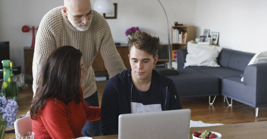 18. Geburtstag vom Kind: Eltern sitzen mit ihrem Sohn vor dem Laptop und reden