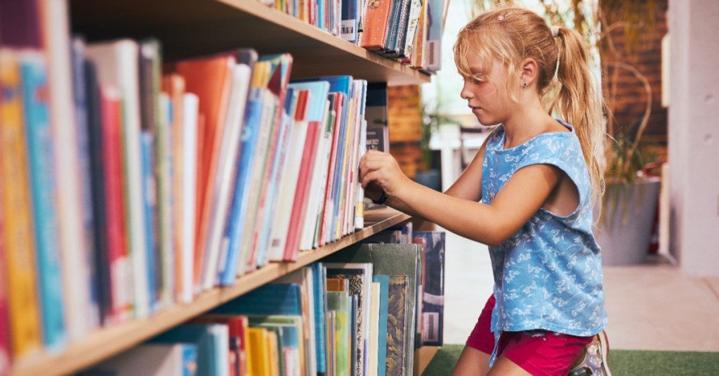 Mädchen greift ein Buch aus einem Bücherregal