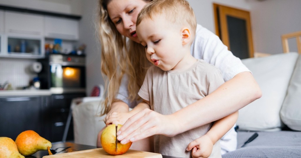 Mutter schneiden gemeinsam mit ihrem Kind einen Apfel