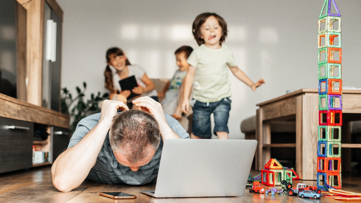 Vater versucht zu Hause am Laptop zu arbeiten, während seine Kinder im Hintergrund spielen