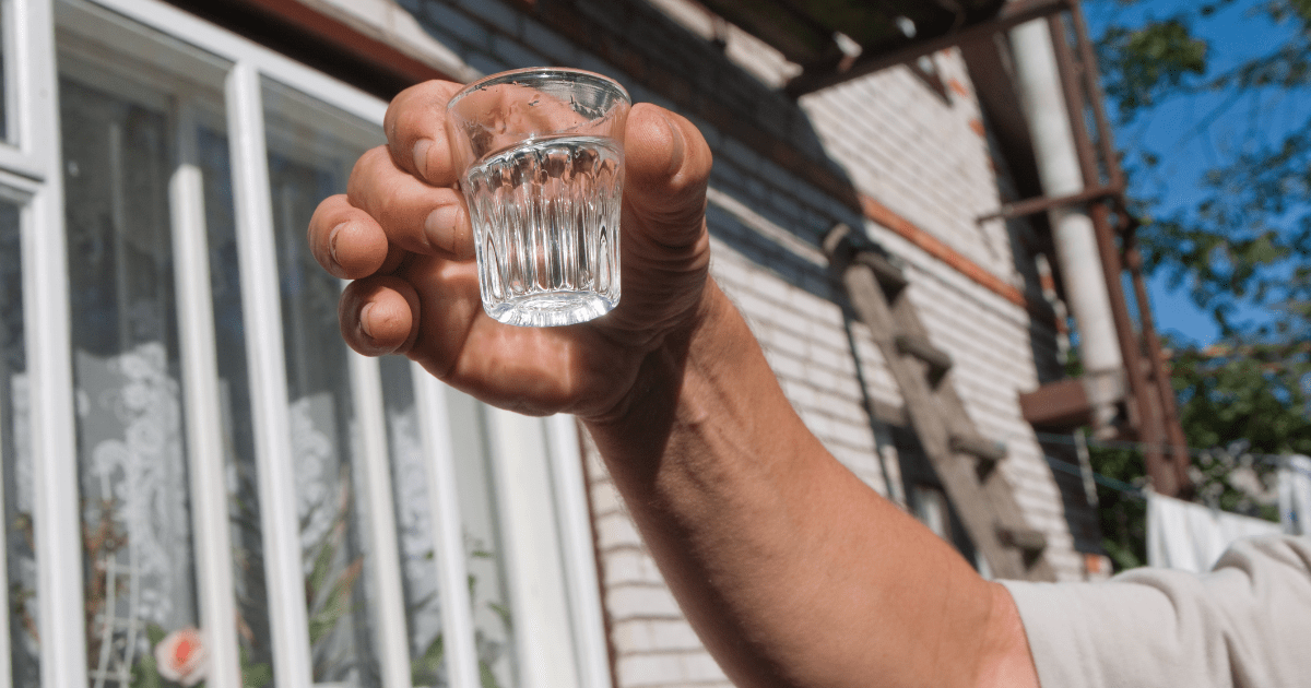 Eine Person hÃ¤lt ein Schnapsglas mit Wodka in die Luft.