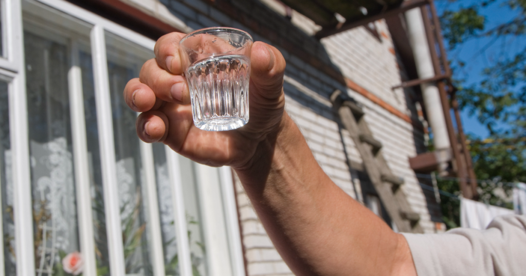 Eine Person hält ein Schnapsglas mit Wodka in die Luft.