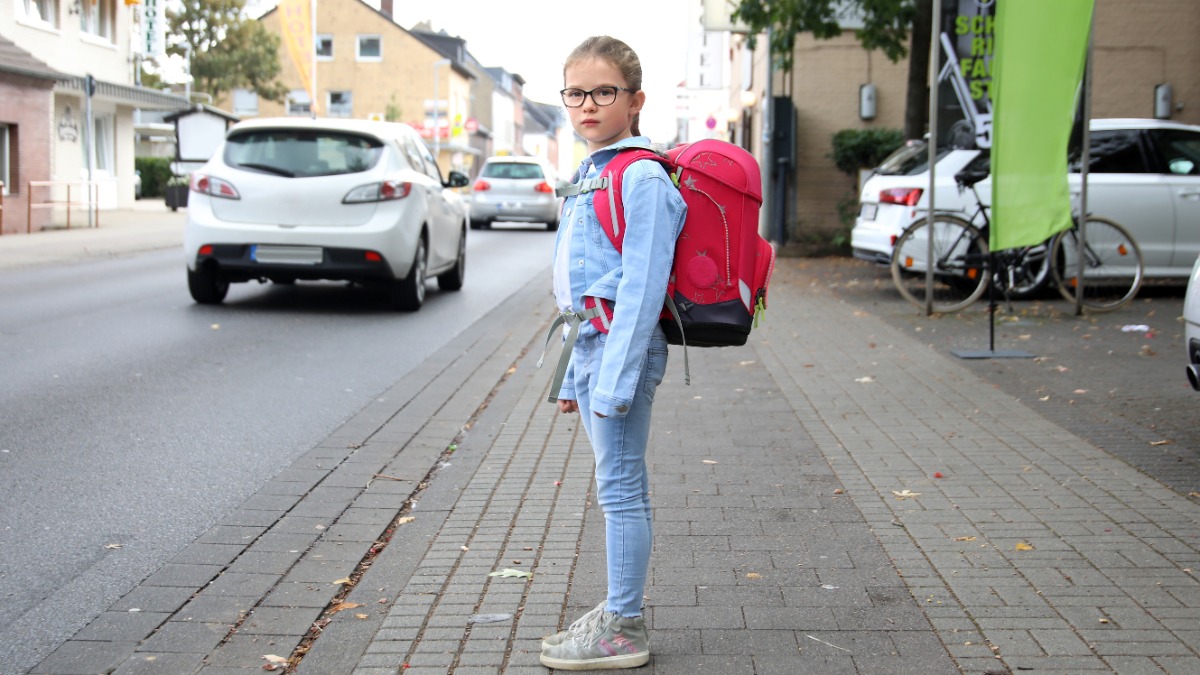 sicherer Schulweg: ein Mädchen möchte eine viel befahrene Straße überqueren