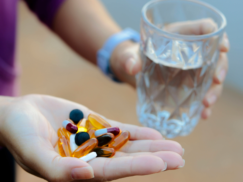 Eine Hand hält viele verschiedene Tabletten, die andere ein Glas Wasser.