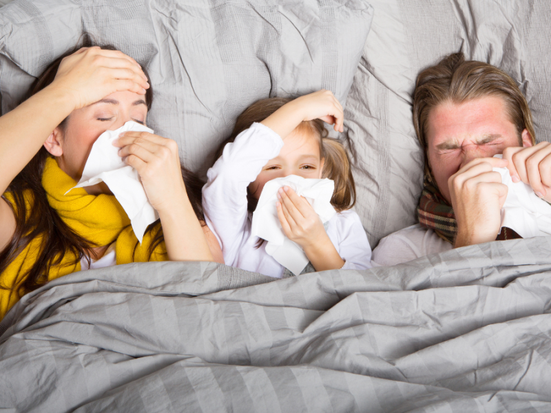 Mutter, Vater und Kind liegen krank im Bett.